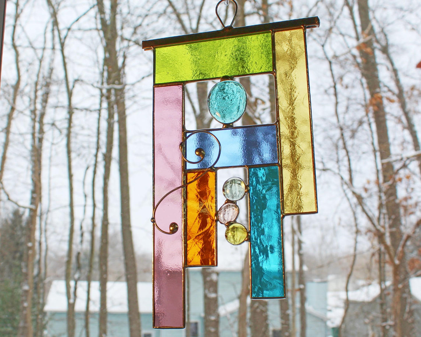 Handcrafted geometric stained glass window hanging in soft tones.