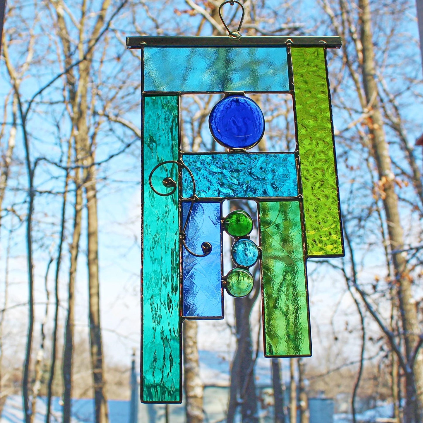 Handcrafted geometric stained glass window hanging in tranquil tones of blue and green.