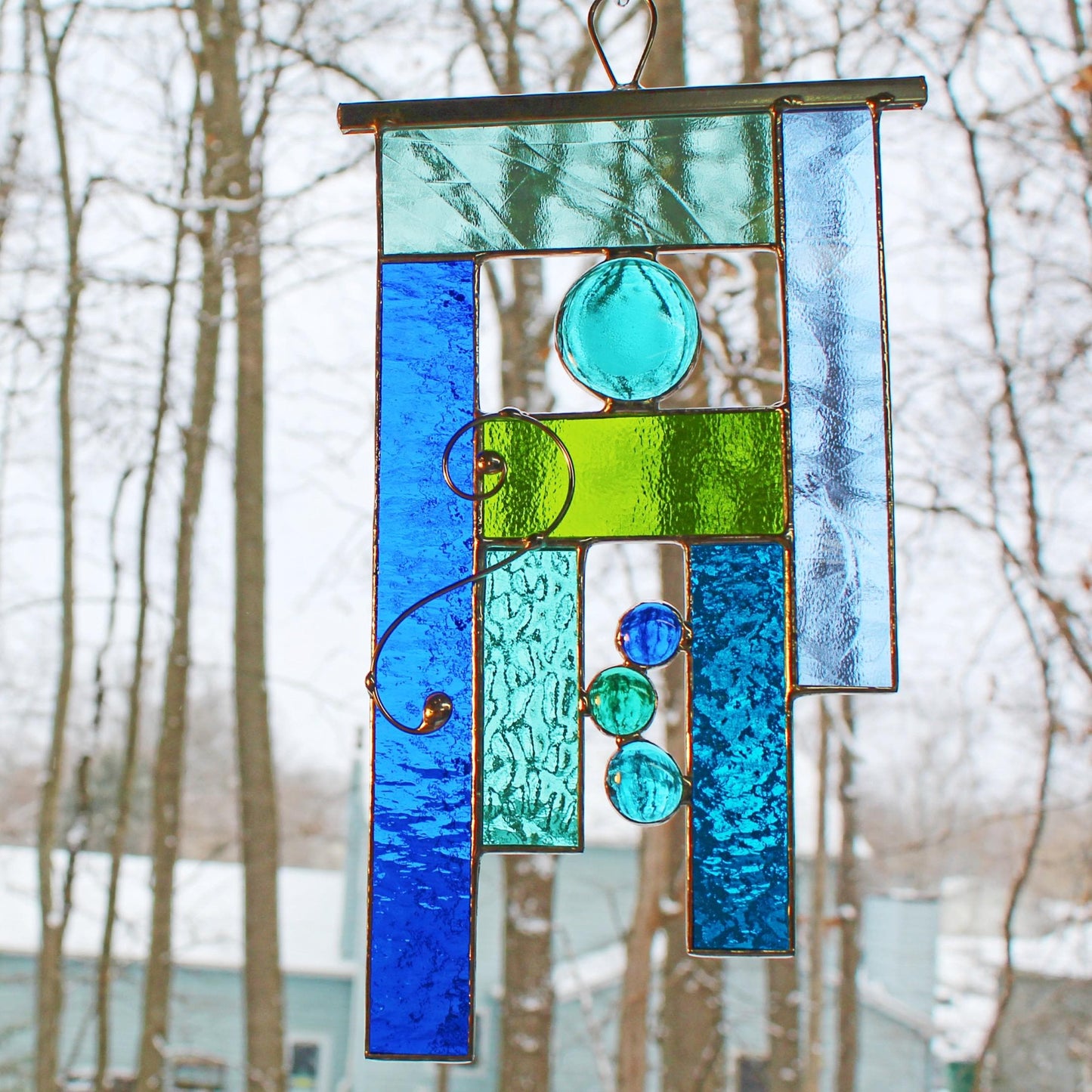 Handcrafted geometric stained glass window hanging in tranquil tones of green and blue.